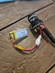 A compact rocket altimeter assembly next to a small lithium polymer battery and JST connector.