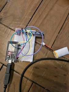A breadboard prototype with an ESP32 development board, sensor board, display, battery, and jumper wires.
