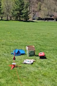 A model rocket launch setup on a grassy field with launch gear nearby.